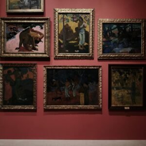 A collection of framed classic paintings on a red wall in a gallery setting.