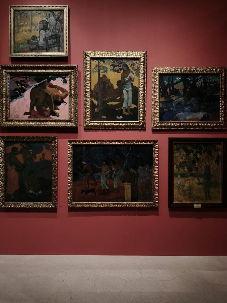 A collection of framed classic paintings on a red wall in a gallery setting.